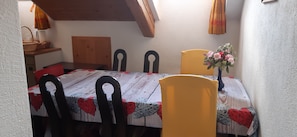 Zona de dinar amb taula per a quatre, caires de fusta, un ram de flors i un panell de fusta al capçal del llit.