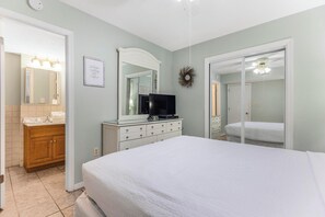 Een slaapkamer met een bed, een dressoir, een televisie en een badkamer met een spiegel en wastafel.