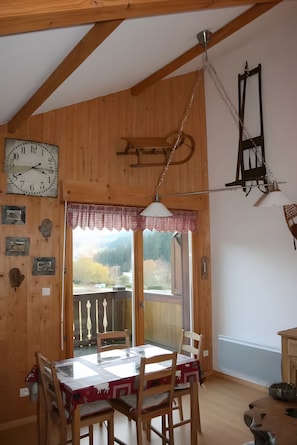 Ein Holzinterieur mit einem Esstisch, Stühlen, einer Hängeleuchte und einer Wanduhr.