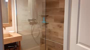 Eine gläserne Duschkabine, ein Holzboden, ein weißes Waschbecken mit Holzablage und ein Spiegel über dem Waschbecken.