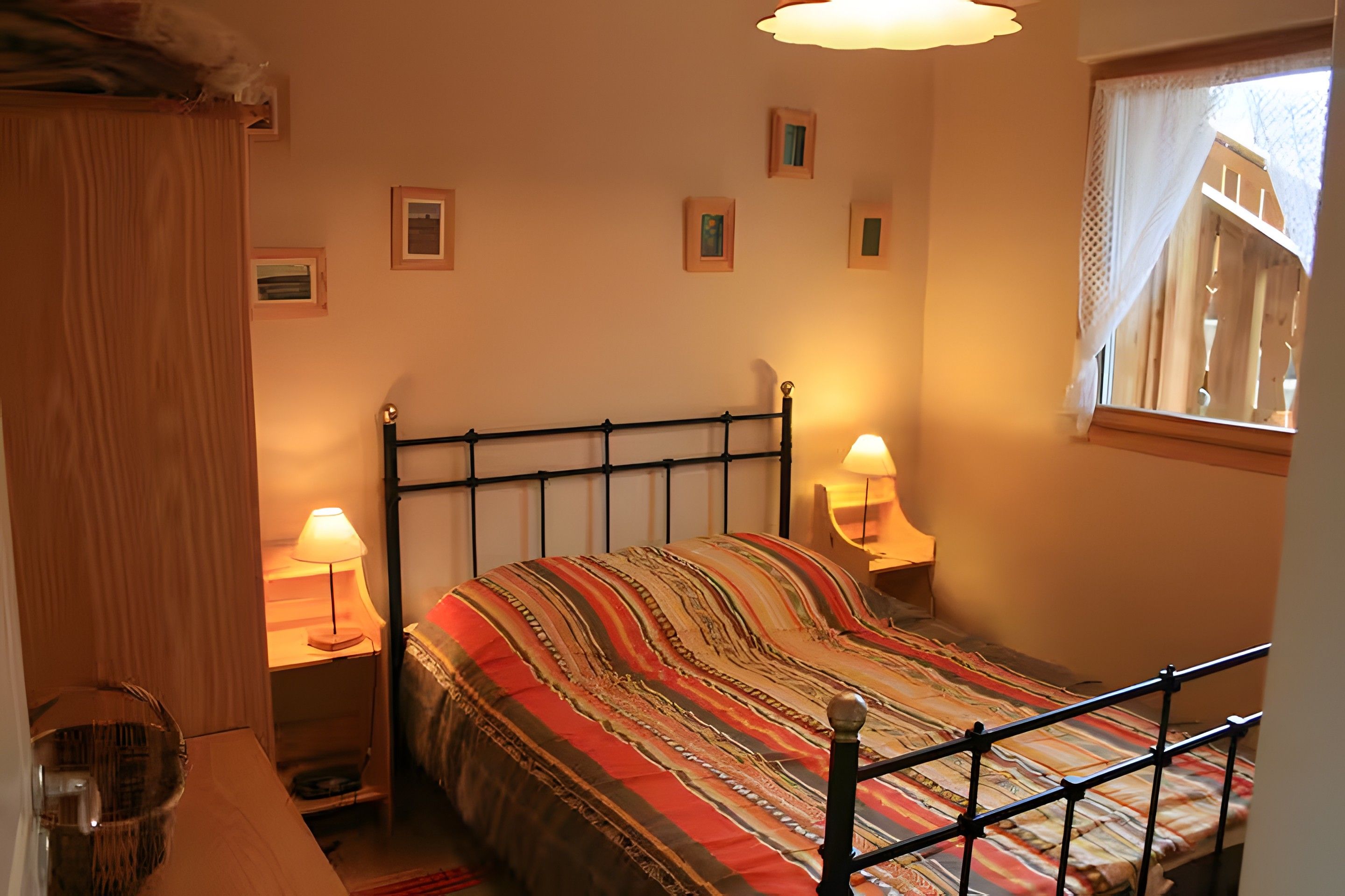 Ein Schlafzimmer mit einem Bett, zwei Nachttischlampen, einem Fenster mit Vorhang und einem kleinen Nachttisch.