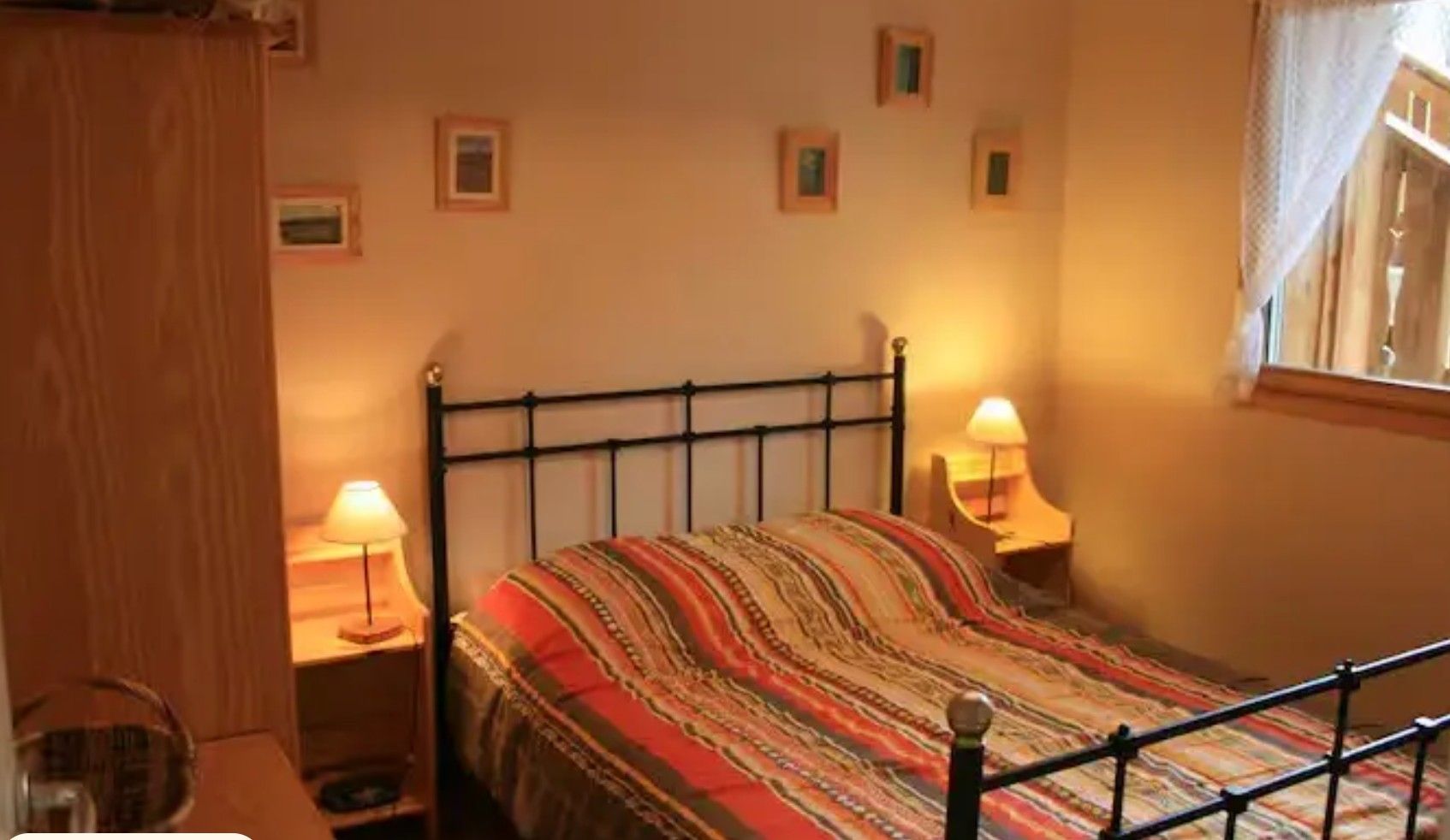 Ein Schlafzimmer mit einem Bett, zwei Nachttischen mit Lampen, einem Holzschrank und einem Fenster mit Vorhängen.