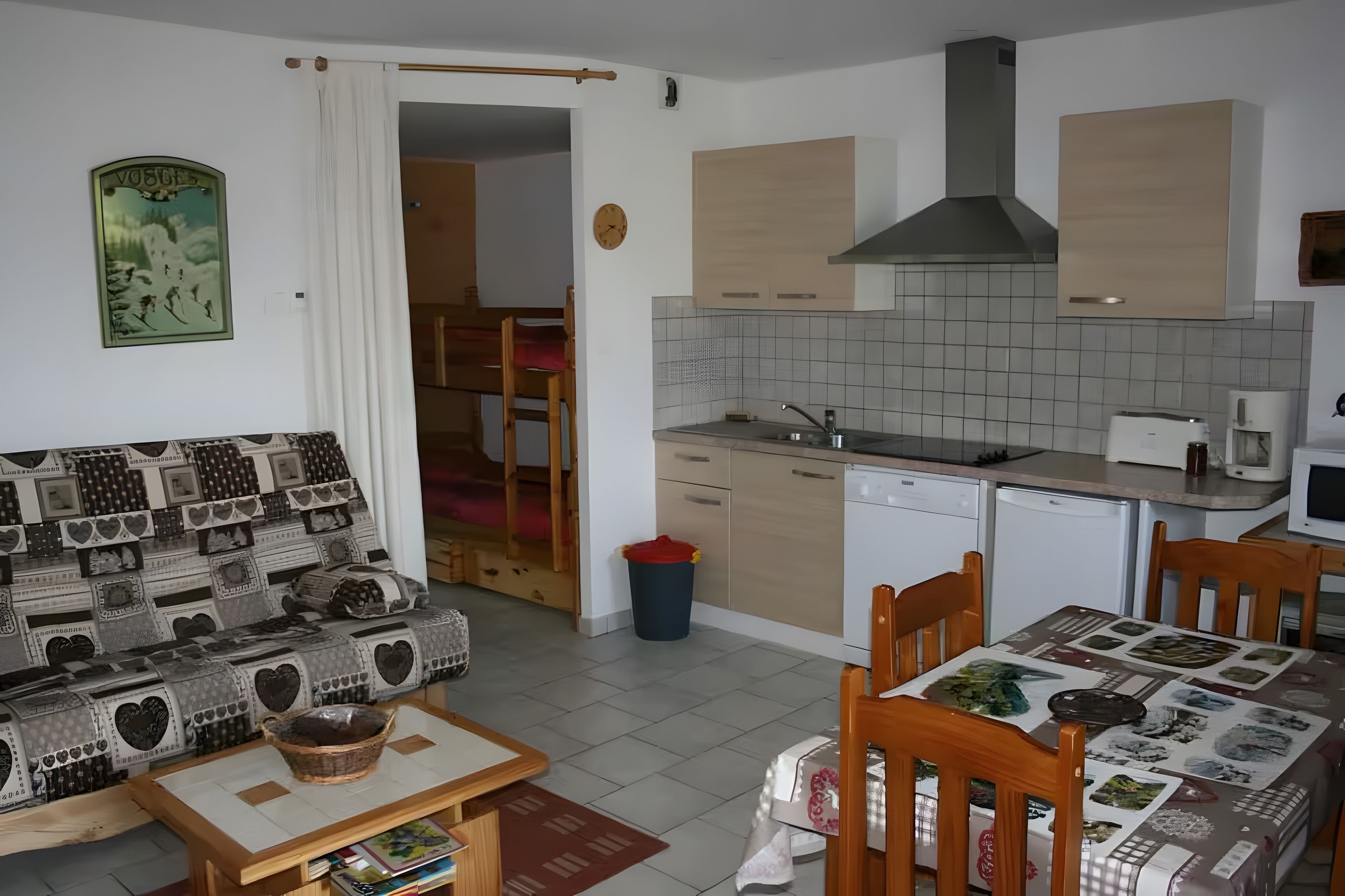 Ein kompakter Wohnraum mit Küchenzeile, Essbereich und einer Couch mit gemustertem Bezug.