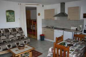 Ein kompakter Wohnraum mit Küchenzeile, Essbereich und einer Couch mit gemustertem Bezug.