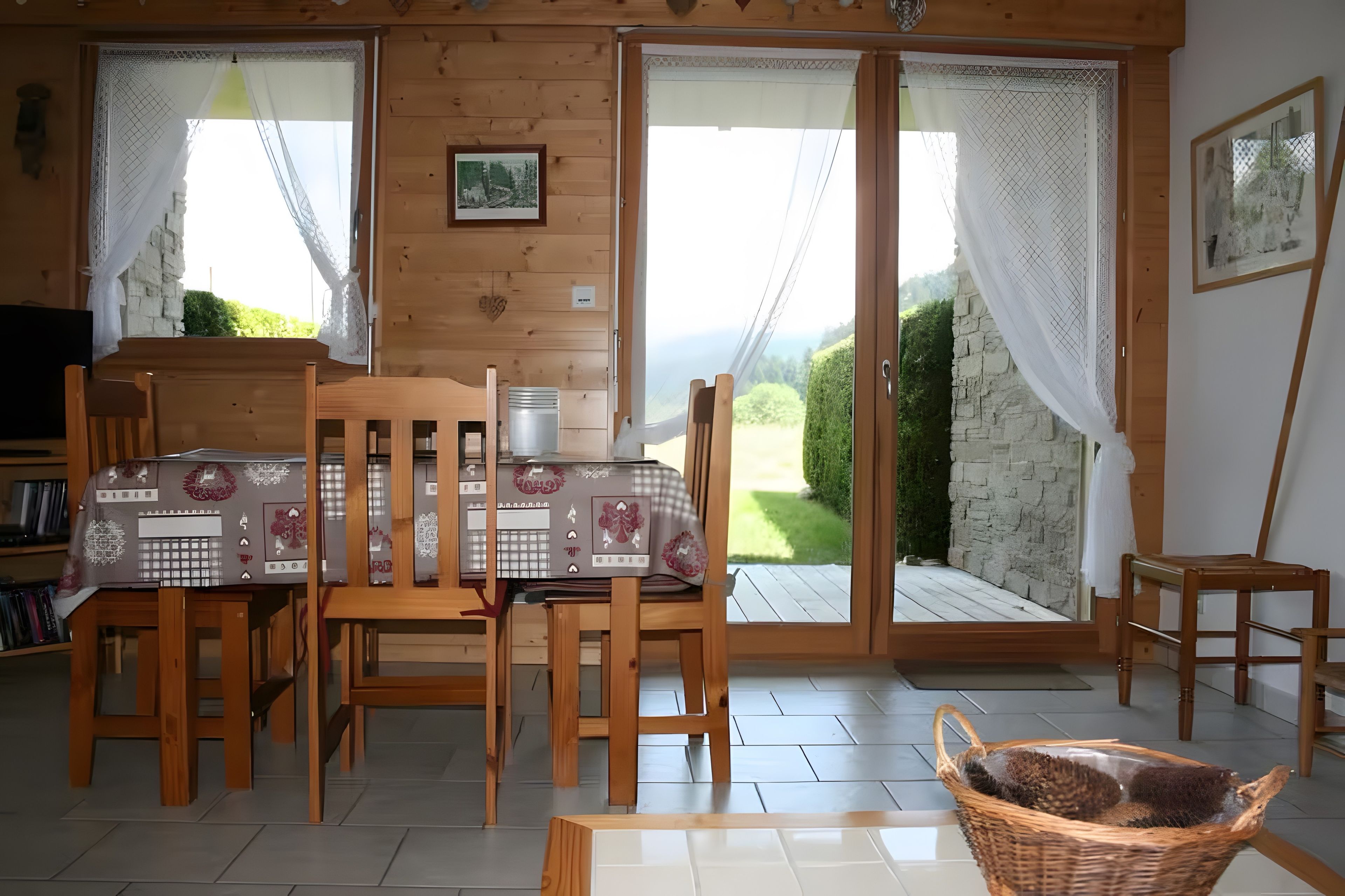 Un intérieur en bois comprenant une table à manger, des chaises et une vue sur l’extérieur, accessible par des portes vitrées.
