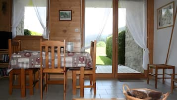 Un intérieur en bois comprenant une table à manger, des chaises et une vue sur l’extérieur, accessible par des portes vitrées.
