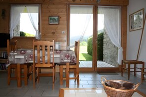 Un intérieur en bois comprenant une table à manger, des chaises et une vue sur l’extérieur, accessible par des portes vitrées.