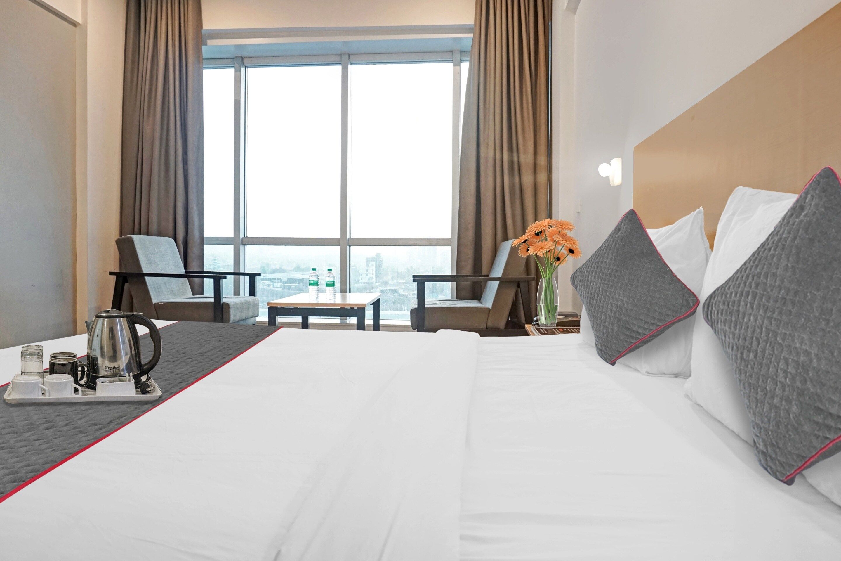 Una habitación de hotel con una cama grande, dos sillones, una mesita, una cafetera y un jarrón con flores.