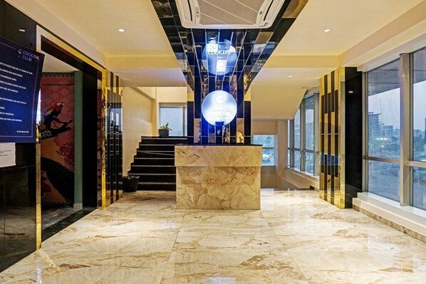 Un moderno vestíbulo de hotel con piso de mármol, un mostrador de recepción central y una escalera que conduce a plantas superiores.