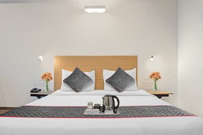 A hotel room with a bed, two nightstands, a bedside table, a kettle, a tray with cups and a teapot, and two vases with flowers.