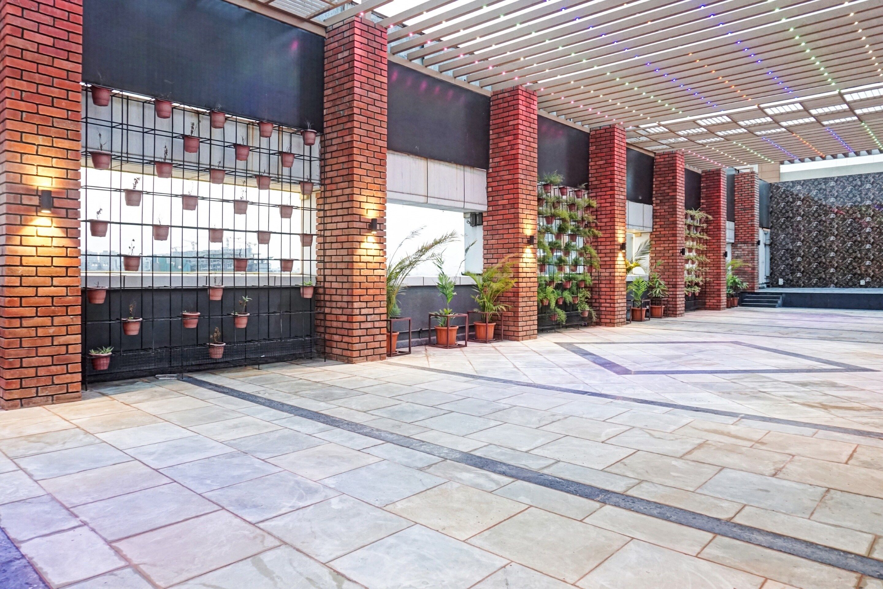 A covered outdoor area with tiled flooring, brick pillars, and potted plants.