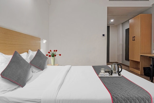 Una habitación de hotel con una cama, una mesita de noche, un florero con flores, una cafetera y un armario.