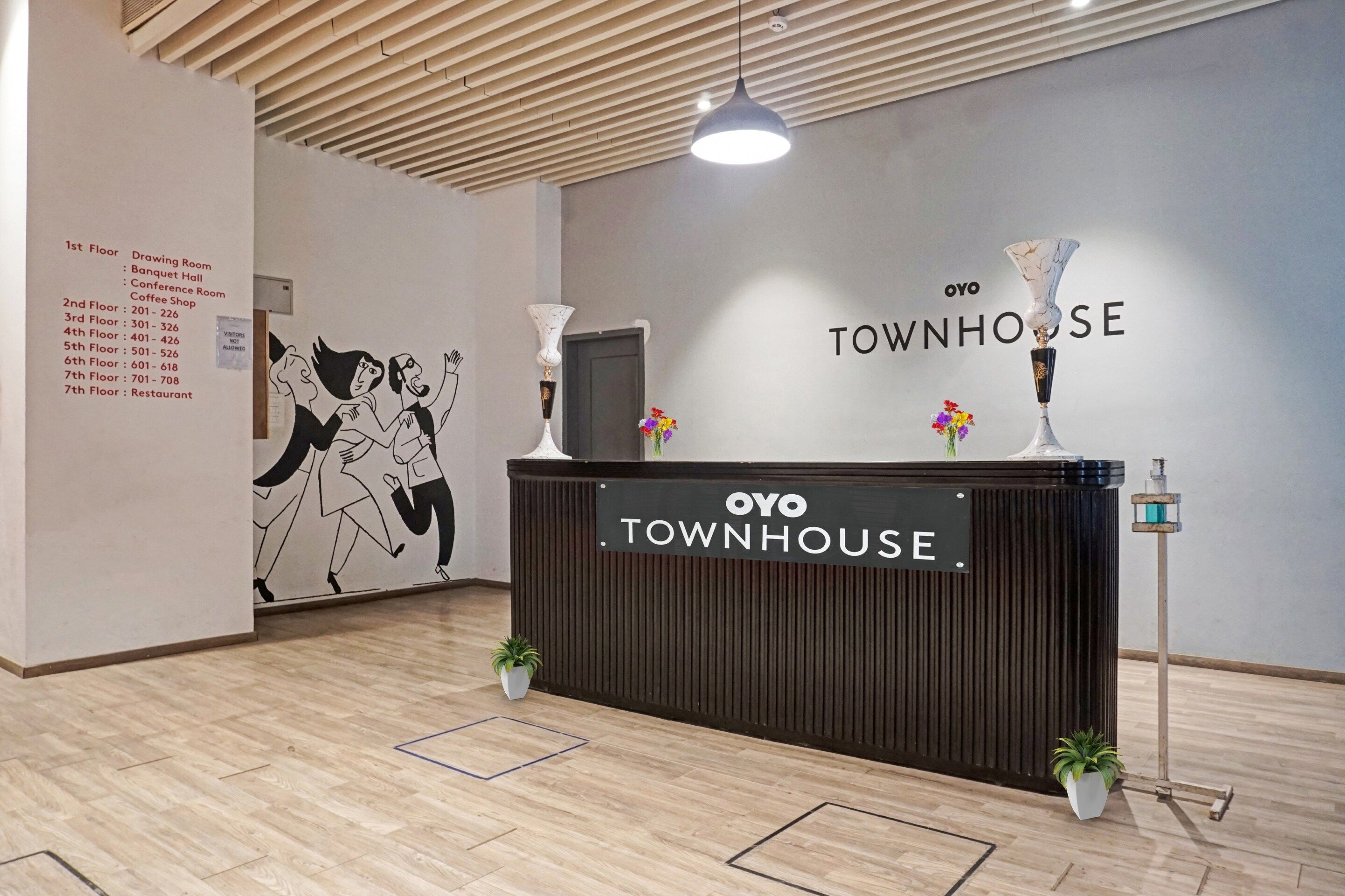 Un comptoir d’accueil avec une enseigne indiquant « OYO TOWNHOUSE » et une liste des noms et numéros des étages affichée sur le mur.