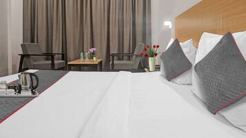 A hotel room with a bed, two chairs, a small table with a vase of flowers, and a tray with a kettle and cups.