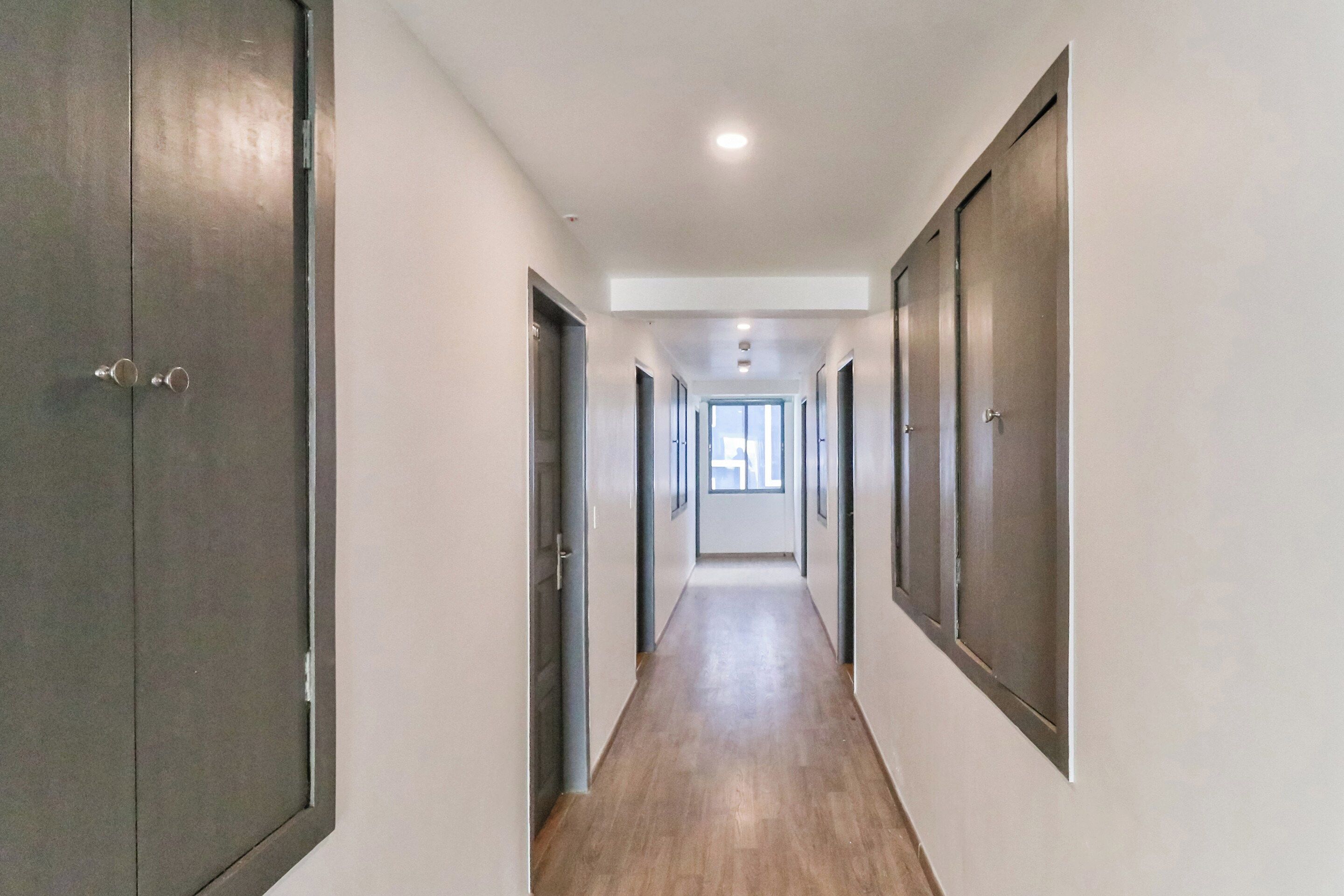 Un pasillo con puertas a ambos lados, que conduce a una habitación con ventana.
