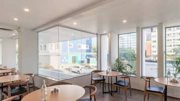 A modern interior with round tables and chairs, large windows with city views, and a glass partition.