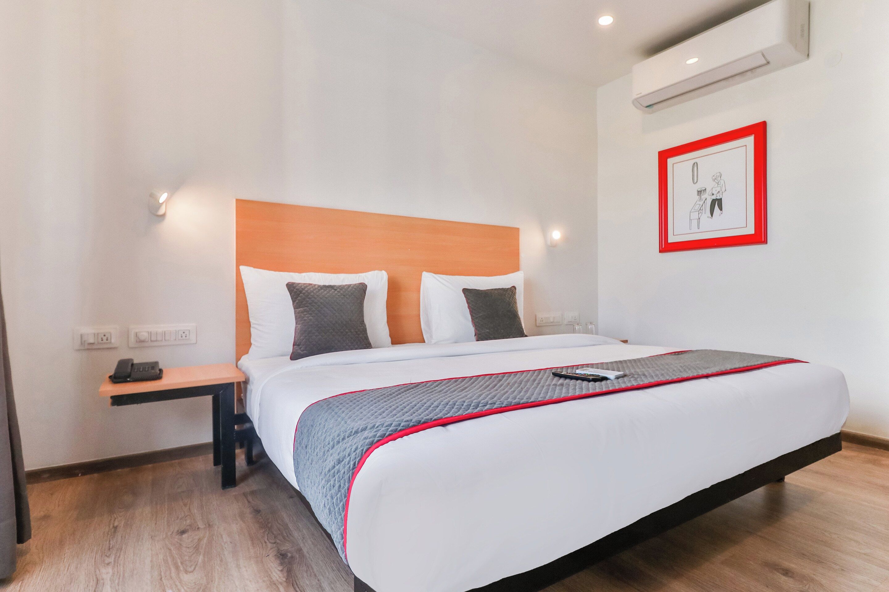 Una habitación de hotel con cama, mesita de noche y aire acondicionado de pared.
