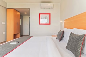 Habitació d'hotel amb un llit, una fotografia emmarcada a la paret, un aparell d'aire condicionat i una porta que condueix a una altra habitació.