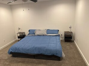 Une chambre à coucher comprenant un lit, deux tables de chevet, un ventilateur de plafond et un sol recouvert de moquette.
