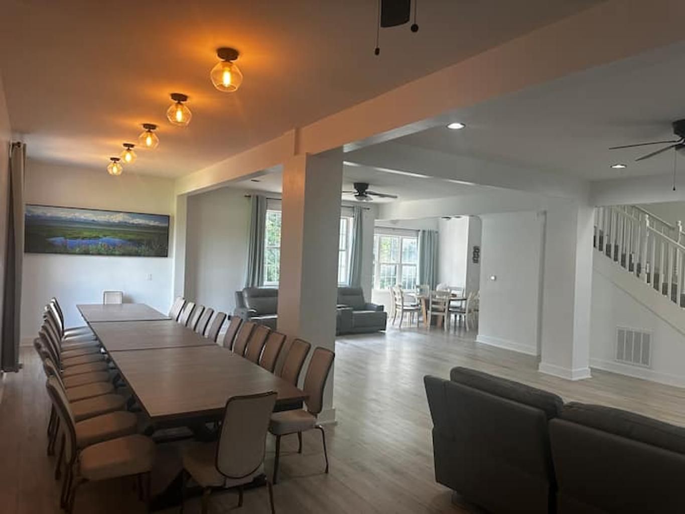 A spacious living area with a long dining table, comfortable seating, and a staircase leading to an upper level.