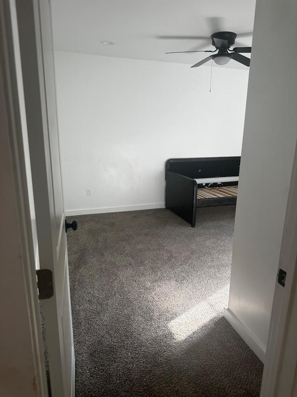 A room with a ceiling fan, a bed, and a carpeted floor.