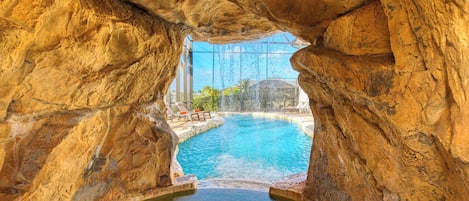 A natural rock formation with a pool and a glass structure.