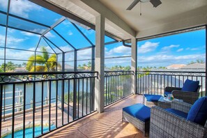 Ein Balkon mit Blick auf einen Swimmingpool und Palmen, ausgestattet mit Korbstühlen und einem Tisch.