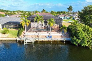 A waterfront property with a swimming pool, palm trees, and a dock. - VRCC Villa Grand Lagoon (Cape Coral)