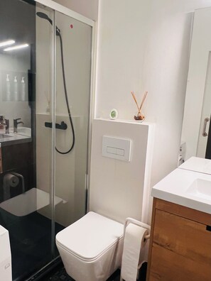 A bathroom with a glass-enclosed shower, a white toilet, a wooden vanity, and a mirror. - Live in Style in Madrid (Madrid)