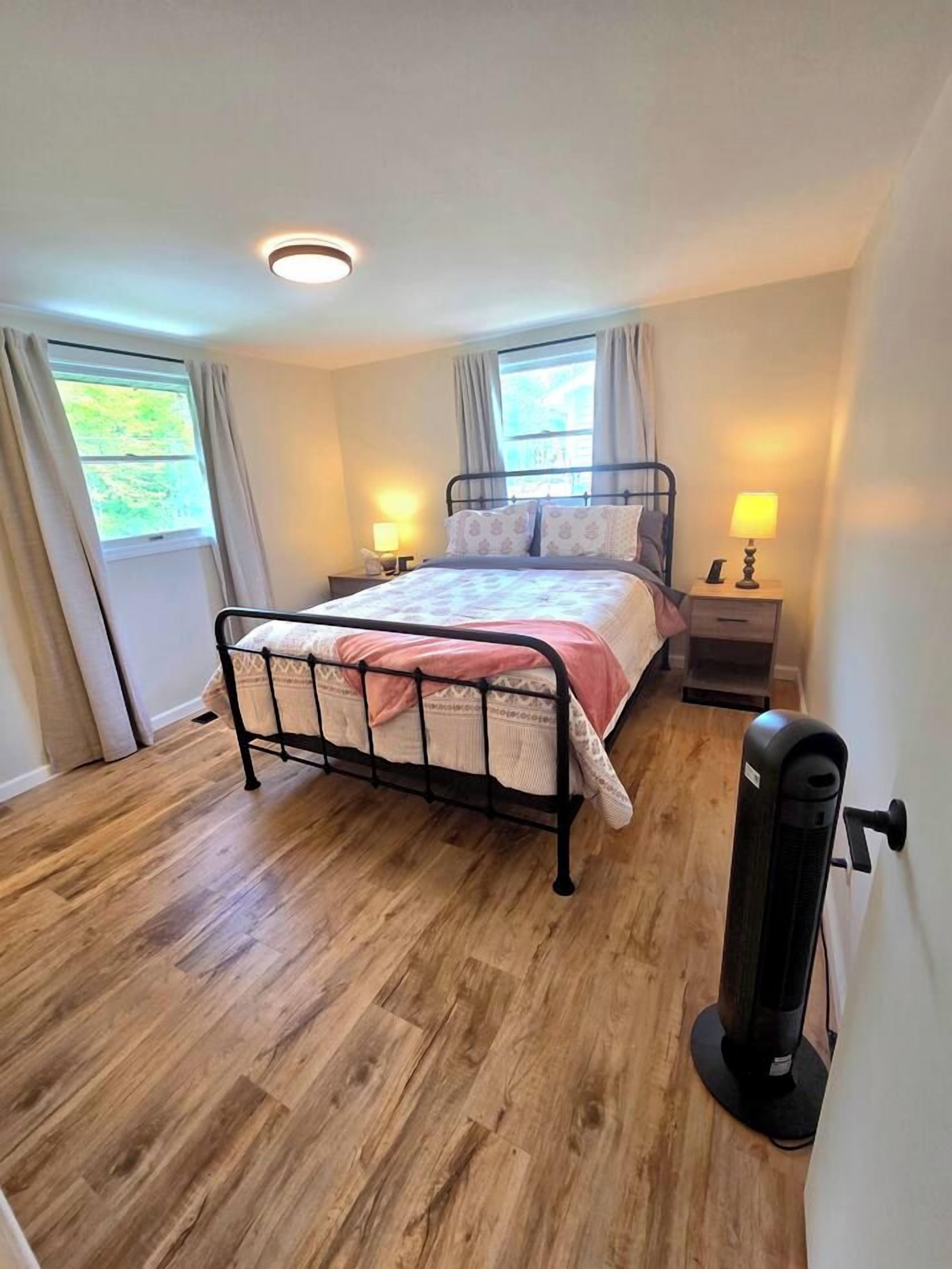 Un dormitorio con cama, lámparas de noche, un calentador y una ventana con cortinas.