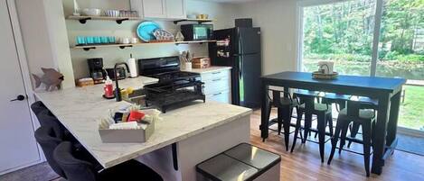 A modern kitchen with a central island, bar stools, a dining table with chairs, and a view of the outdoors.