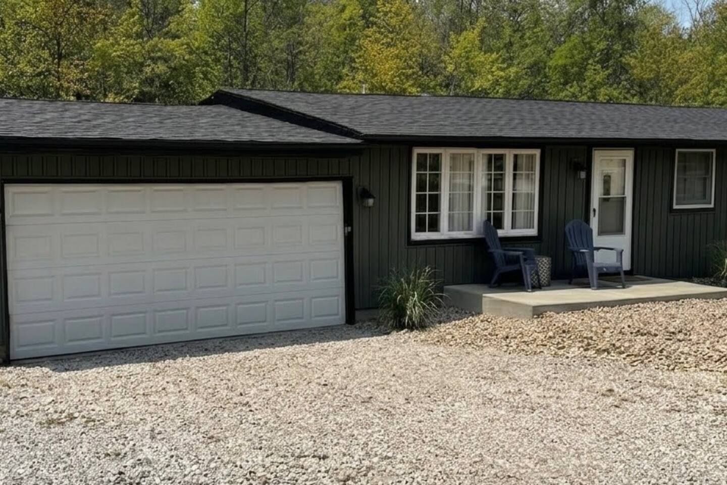 A single-story house with a garage, a front porch with two chairs, and a gravel driveway.
