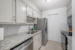 A kitchen with white cabinets, a stainless steel sink, and a built-in dishwasher. - 1st Floor Condo | Walk to Main St | Fireplace (Blowing Rock)