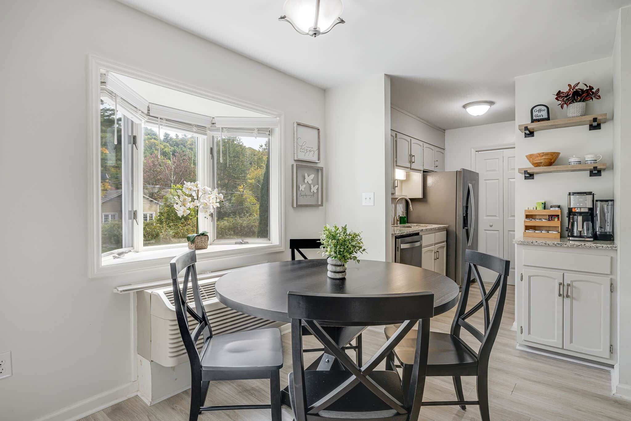 A modern kitchen with a round dining table, white cabinetry, and a view of the outdoors through large windows.
