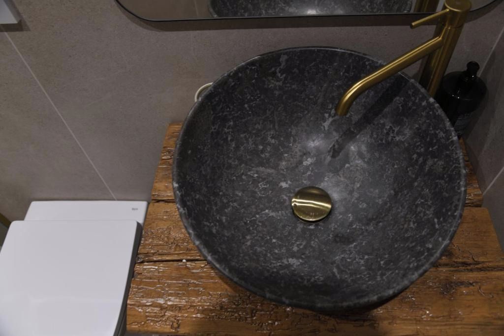 A bathroom with a black marble sink, gold faucet, and a white toilet.