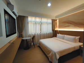 A hotel room with a bed, a TV mounted on the wall, a small round table, and a chair.