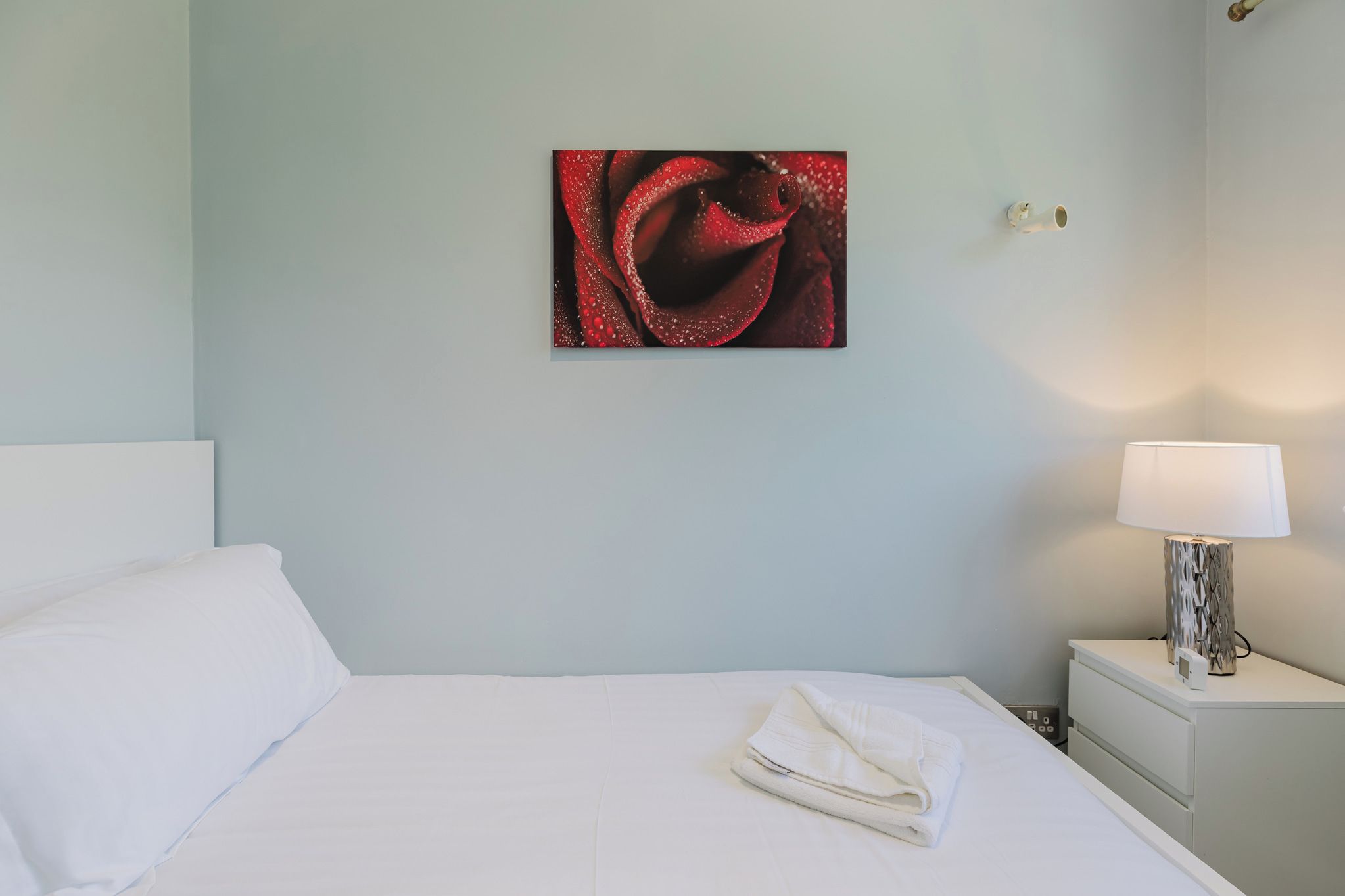 Une chambre d’hôtel avec un lit, une table de chevet avec une lampe et une œuvre d’art accrochée au mur.
