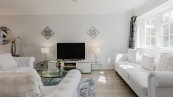 A modern living room with a flat-screen TV, white sofas, a glass coffee table, and decorative wall art.
