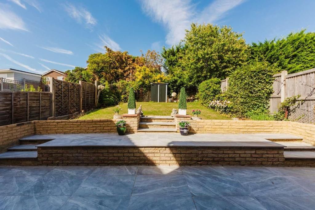 A backyard with a patio, steps leading to a shed, and a wooden fence.