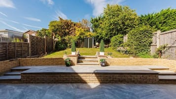A backyard with a patio, steps leading to a shed, and a wooden fence.