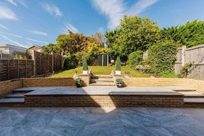 A backyard with a patio, steps leading to a shed, and a wooden fence.