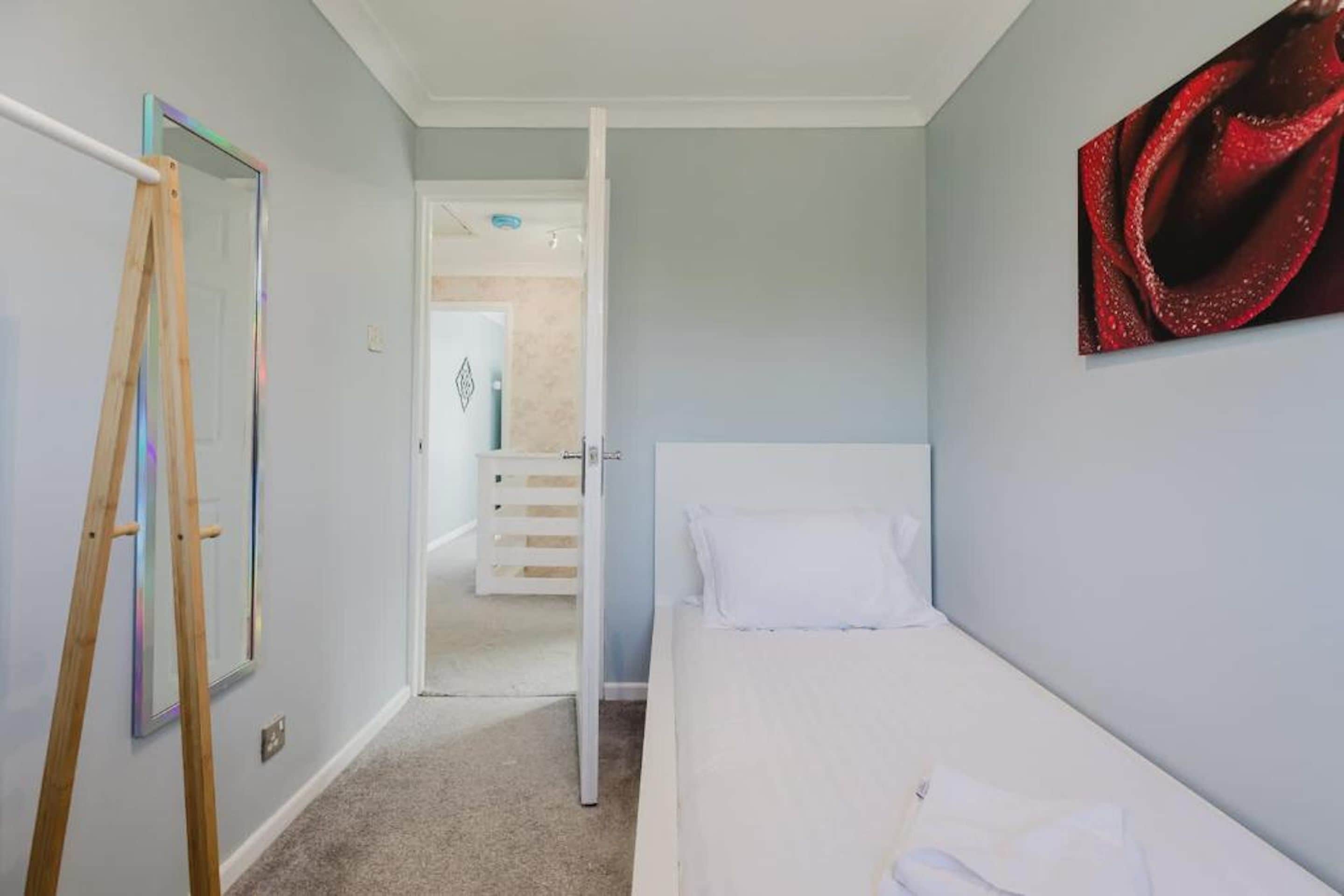 A room with a bed, a door, a white dresser, and a painting on the wall.