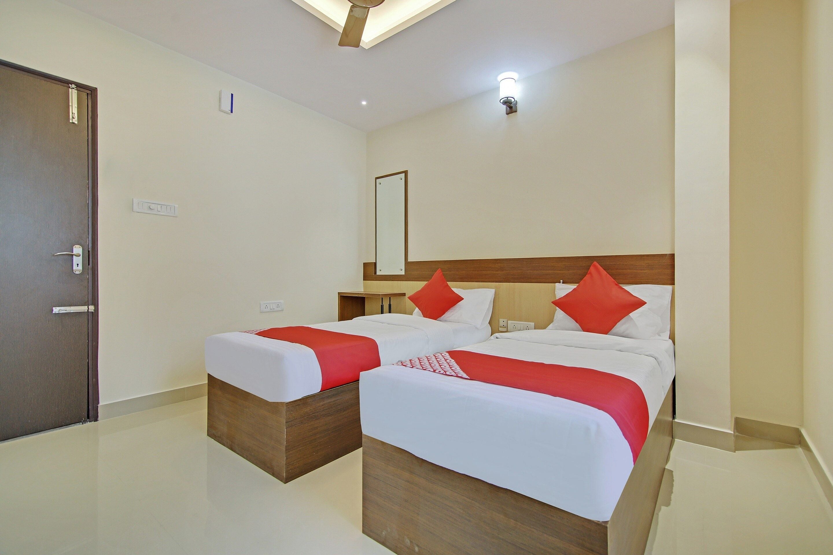 A hotel room with two beds, a wooden headboard, a mirror, and a door.