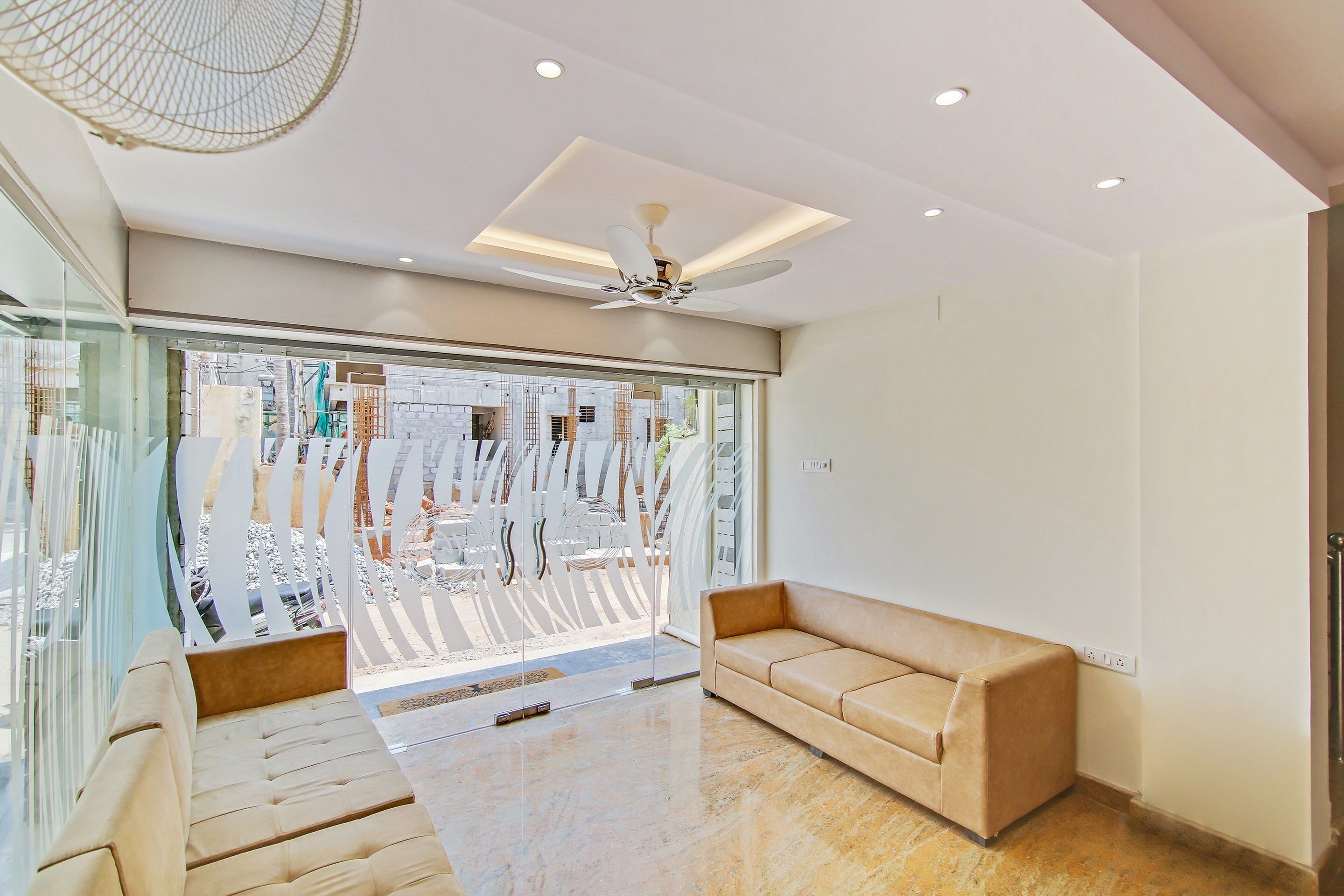 A modern interior with a sofa, a ceiling fan, and a large window with a view of construction outside.