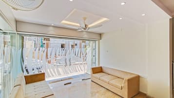A modern interior with a sofa, a ceiling fan, and a large window with a view of construction outside.