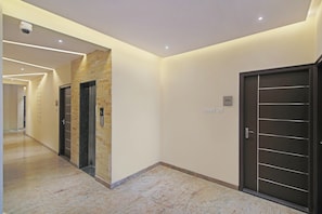 A modern hallway with two elevators, a door with a number plate, and a security camera on the ceiling. - Hotel O With Inn (Bangalore)