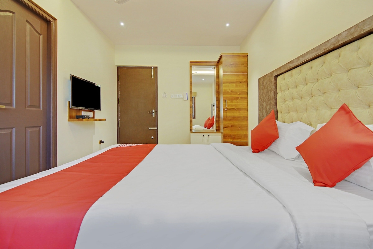 A hotel room with a bed, a television on a stand, a door, and a mirror.