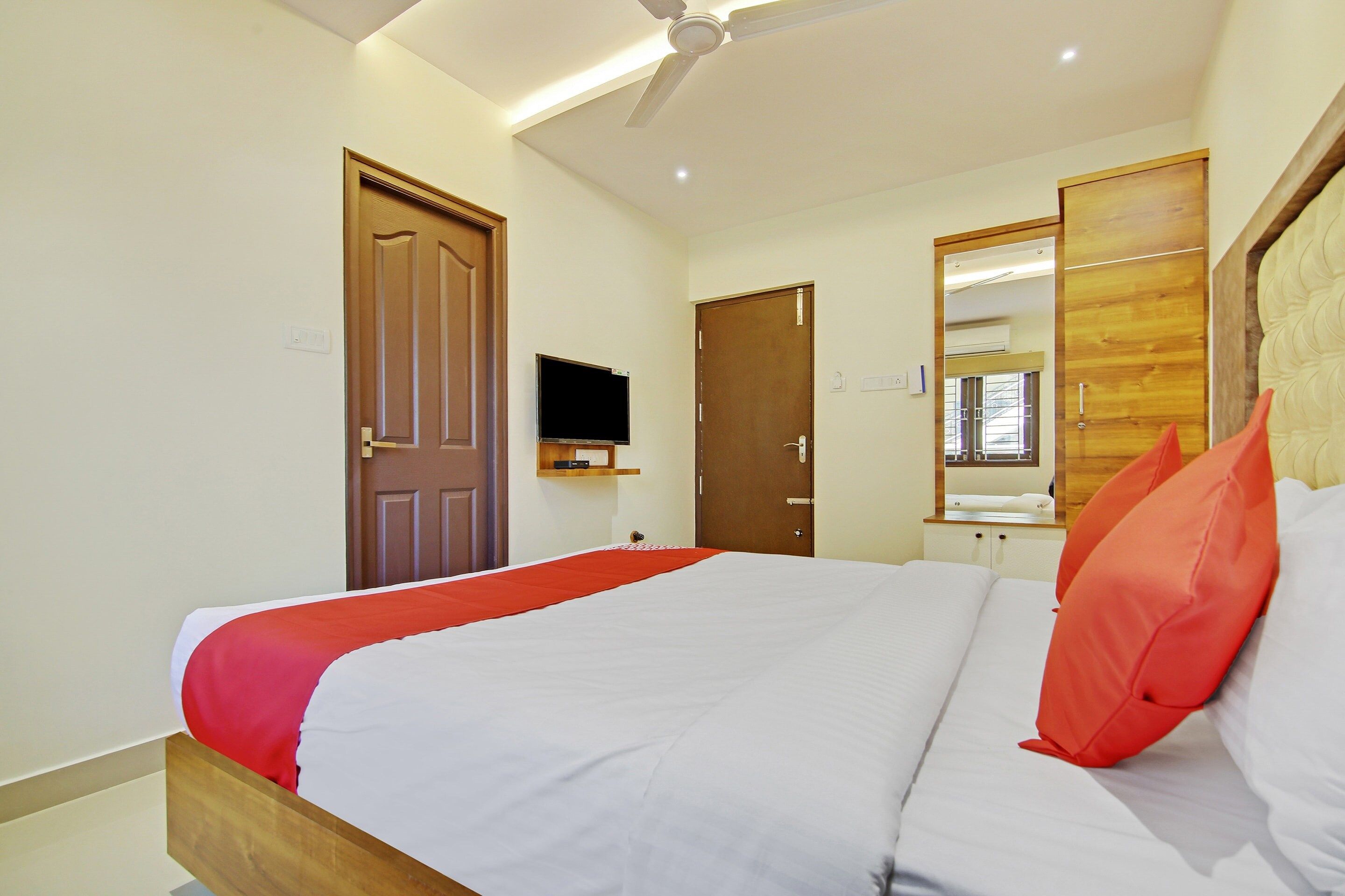 A hotel room with a bed, a television, a mirror, and a ceiling fan.