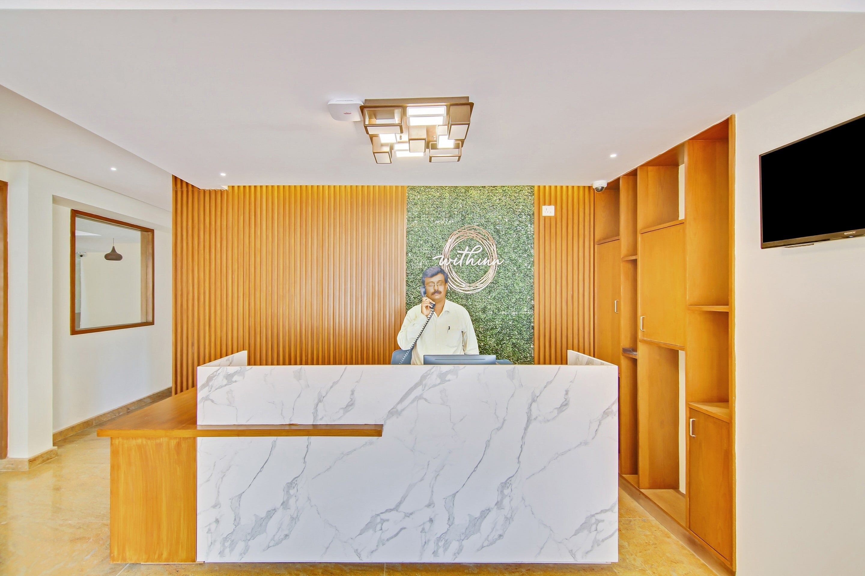 A reception desk with a marble top, a wooden panel wall, and a mounted television on the right.