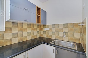 A kitchen with a black countertop, a stainless steel sink, and a tiled backsplash. - Hotel O With Inn (Bangalore)